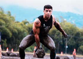 Man performing intense weightlifting during muddy outdoor fitness event.